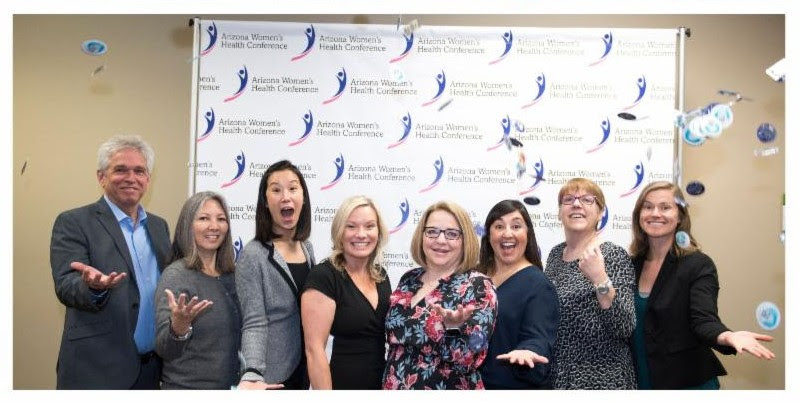 Staff from the Arizona Family Health Partnership stand with wide grins in front of a background of their organization's logo.
